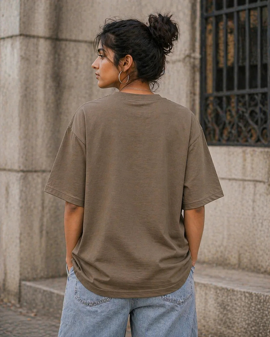 Woman wearing oversized brown t-shirt and light blue jeans, standing outdoors, back view