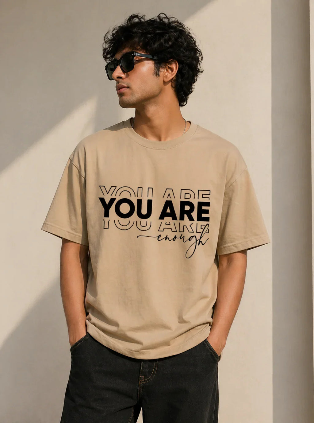 Man wearing beige oversized t-shirt with 'YOU ARE enough' print, casual streetwear style