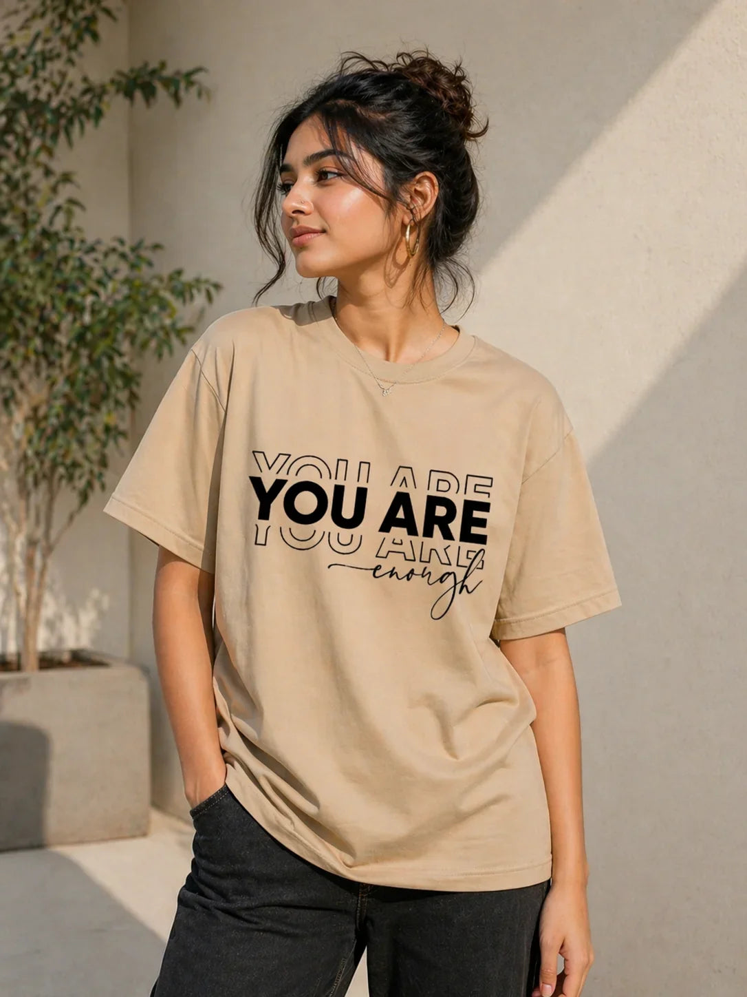 Woman wearing oversized beige t-shirt with 'You Are Enough' print, casual streetwear style