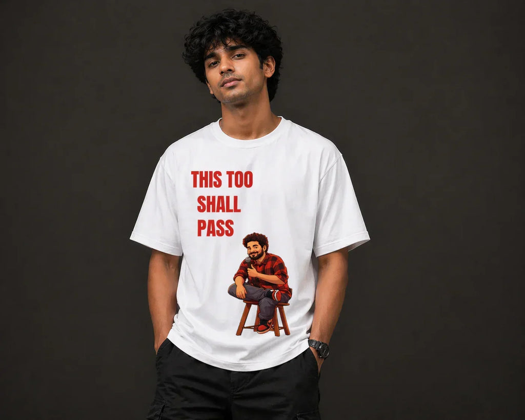 Man wearing oversized white t-shirt with cartoon graphic and 'This Too Shall Pass' text