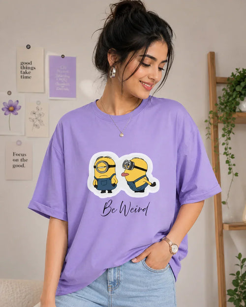 Woman wearing oversized lavender anime t-shirt with cartoon print and 'Be Weird' text