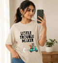 Woman wearing oversized beige t-shirt featuring cartoon cat and mouse riding scooter, text 'Little Trouble Maker'.