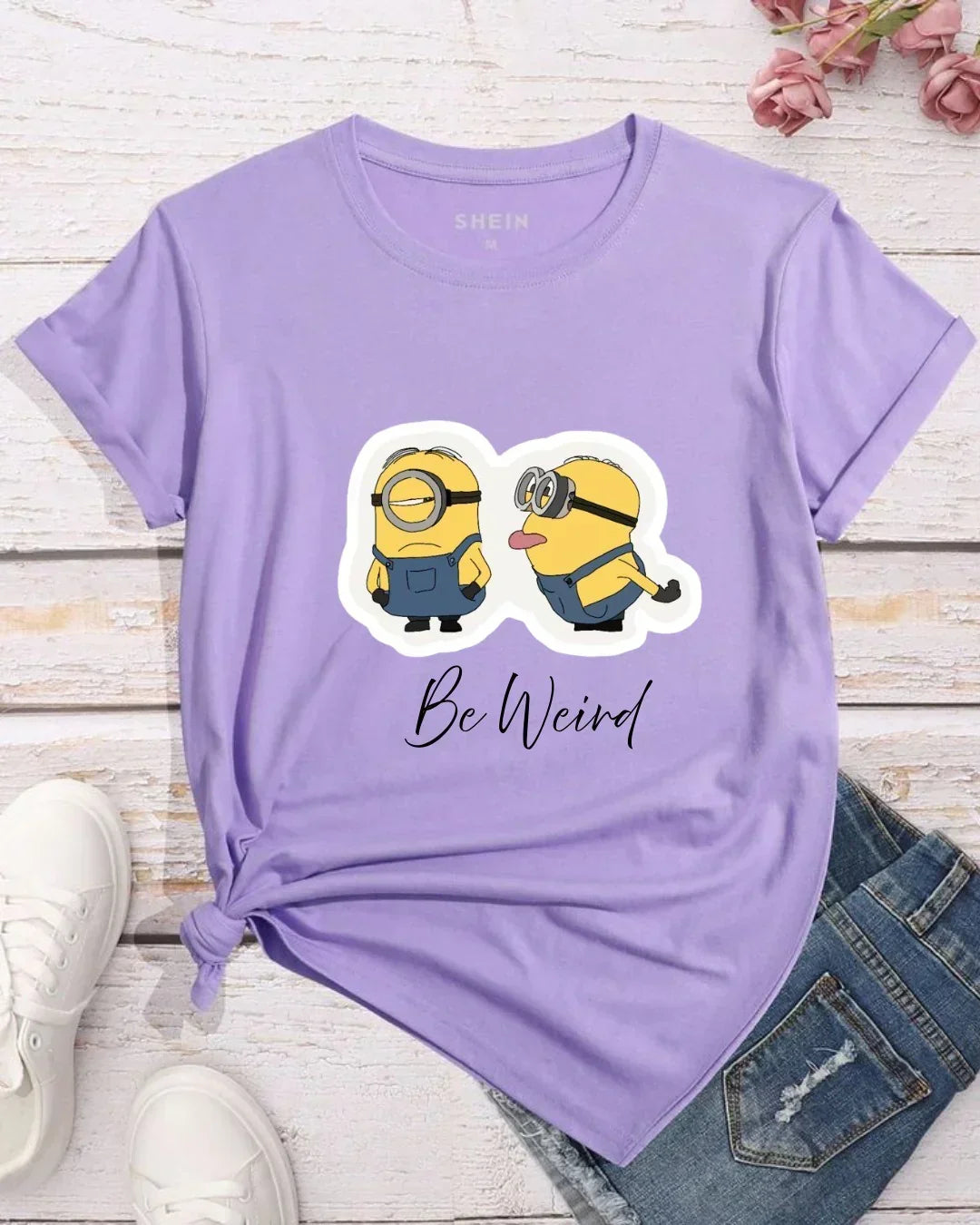 Lavender oversized t-shirt with cartoon minion print and 'Be Weird' text, paired with denim shorts and white sneakers